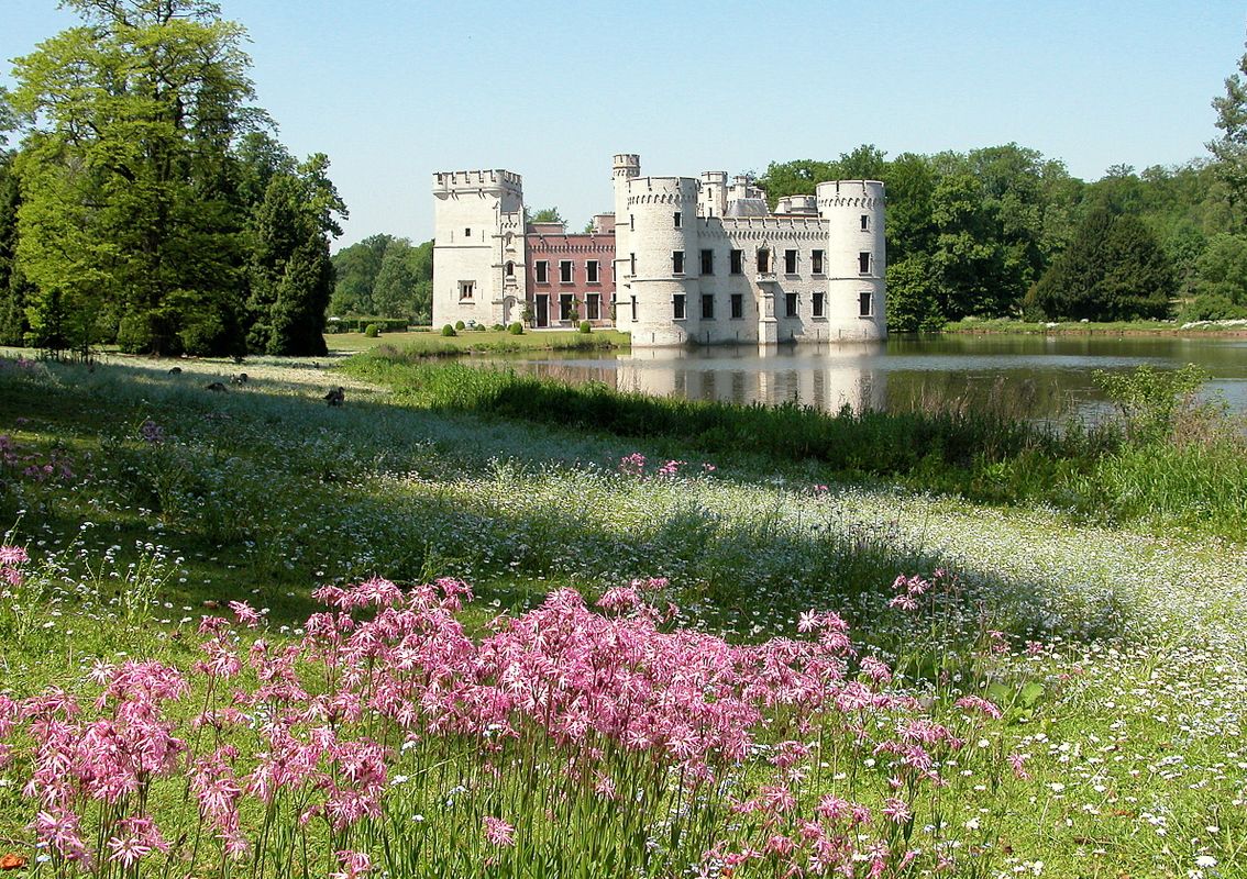 Kasteel van Bouchout naast de vijver in Plantentuin Meise, met torens en bloeiende planten